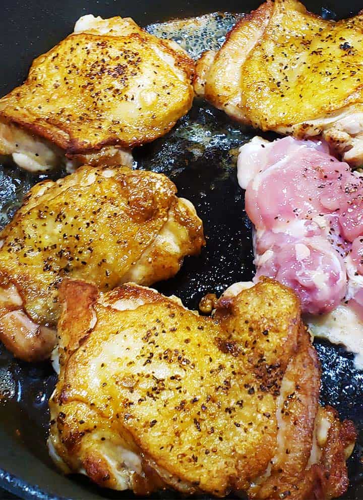 Chicken thighs cooking in cast iron pan