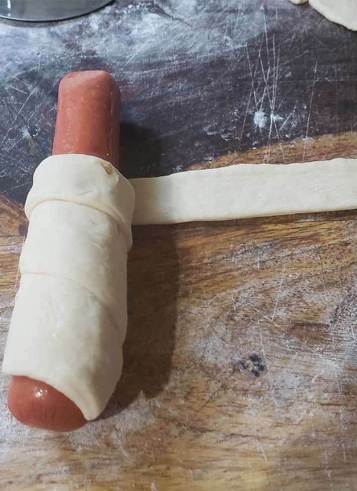 bagel dog being wrapped on wooden cutting board
