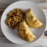 Chicken and broccoli empanada with mexican street corn on a white plate