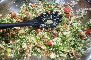 chopped salad in a metal mixing bowl with a black slotted spoon.