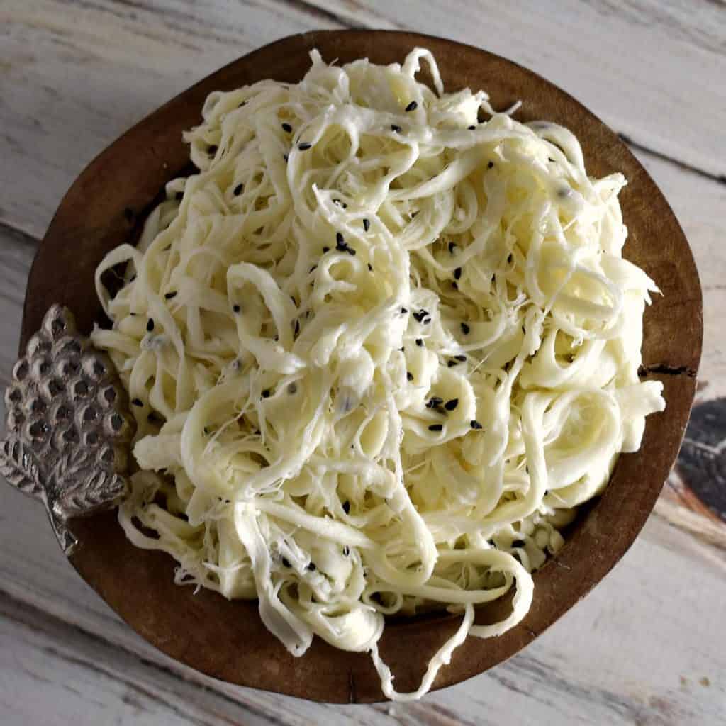 syrian string cheese in a wooden bowl with grape decoration on a white wooden table