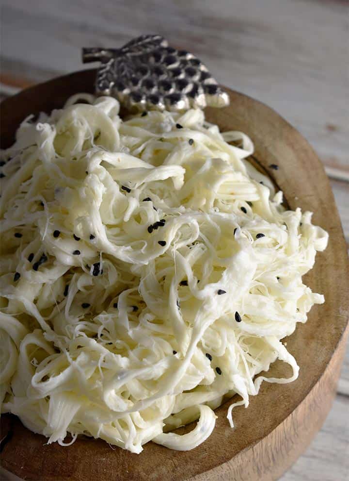 syrian string cheese in a brown bowl with a metal grape decoration against a white wood background