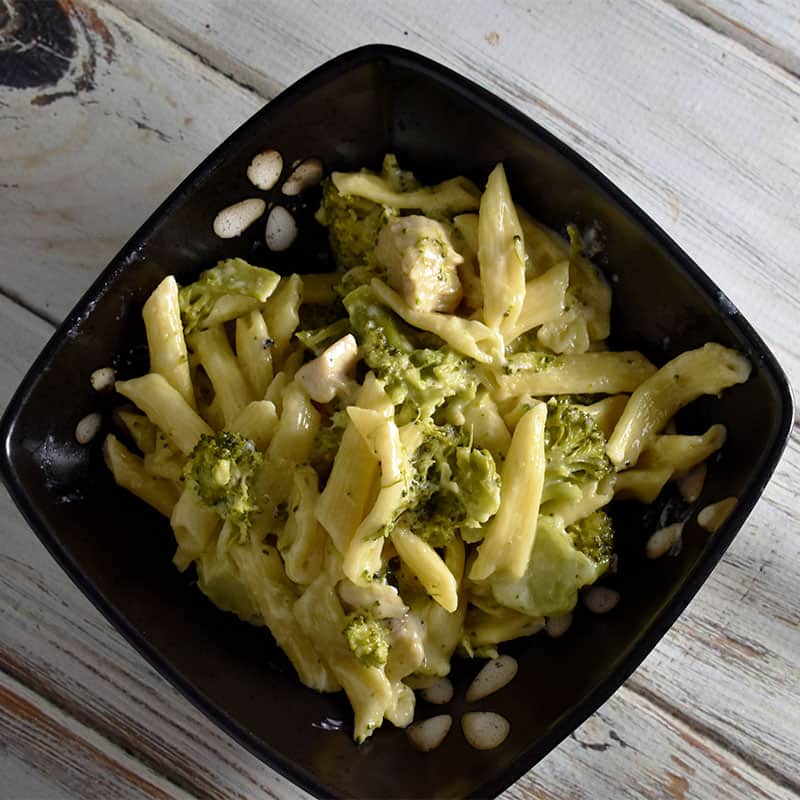 penne pasta with broccoli in a black bowl on a white wooden table