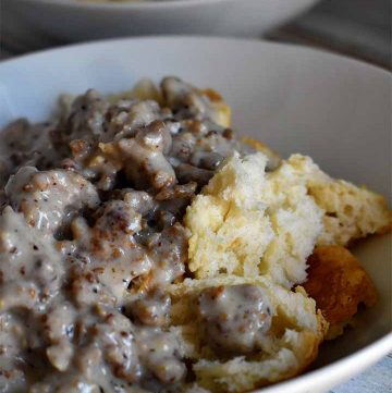 Biscuits and Gravy in a white bowl on a white wooden table