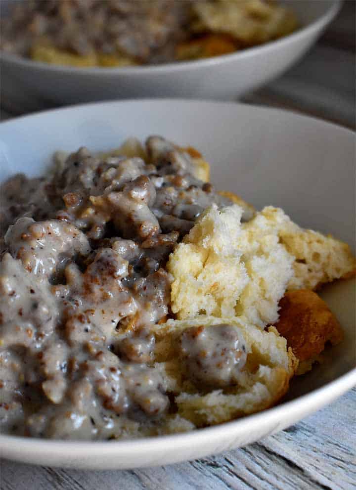 Biscuits and Gravy in a white bowl on a white wooden table