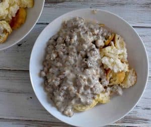 overhead photo of biscuits and gravy in a white bowl on a white wooden table