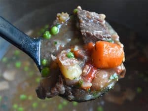 beef stew in black ladle above pot