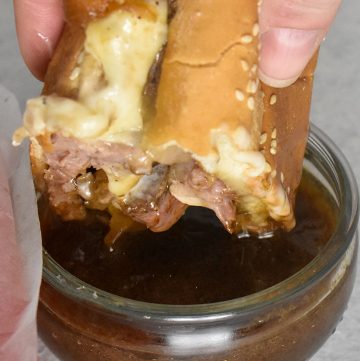 Prime Rib French Dip Sandwich dipped in au jus sauce over a white table