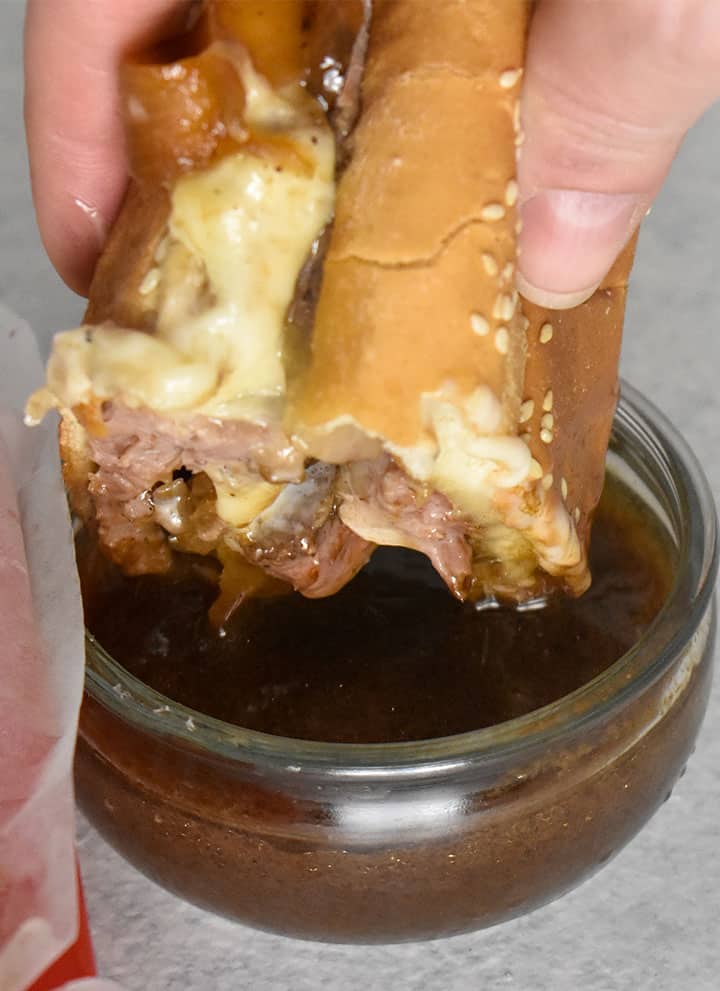 Prime Rib French Dip Sandwich dipped in au jus sauce over a white table