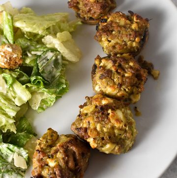 Sausage Stuffed Mushrooms on a white plate with ceasar salad