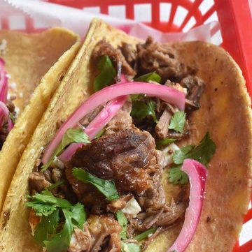 instant pot barbacoa tacos in a corn tortilla with pickled onions and cilantro in a red basket