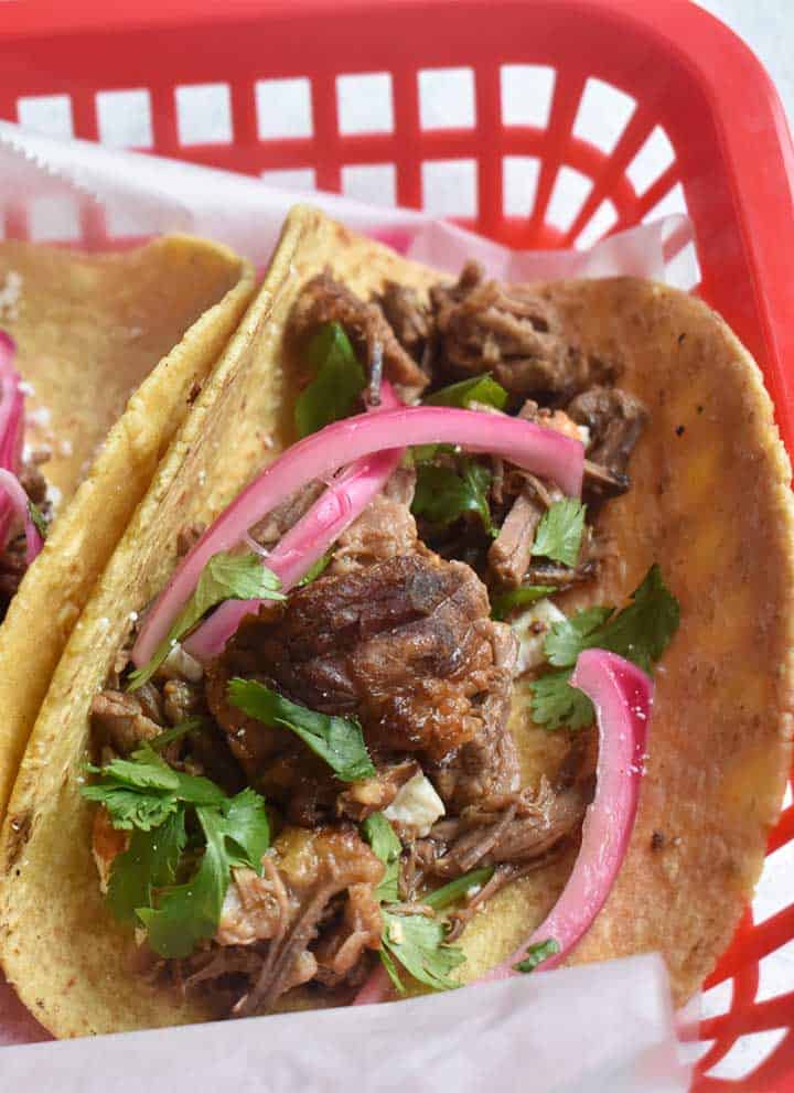 instant pot barbacoa tacos in a corn tortilla with pickled onions and cilantro in a red basket