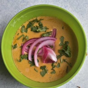 Red Curry Coconut Queso with red onion and cilantro in a green bowl