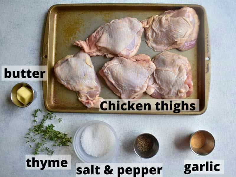 overhead photo of all ingredients on a white table with each ingredient labeled chicken thighs, garlic salt and pepper thyme and butter