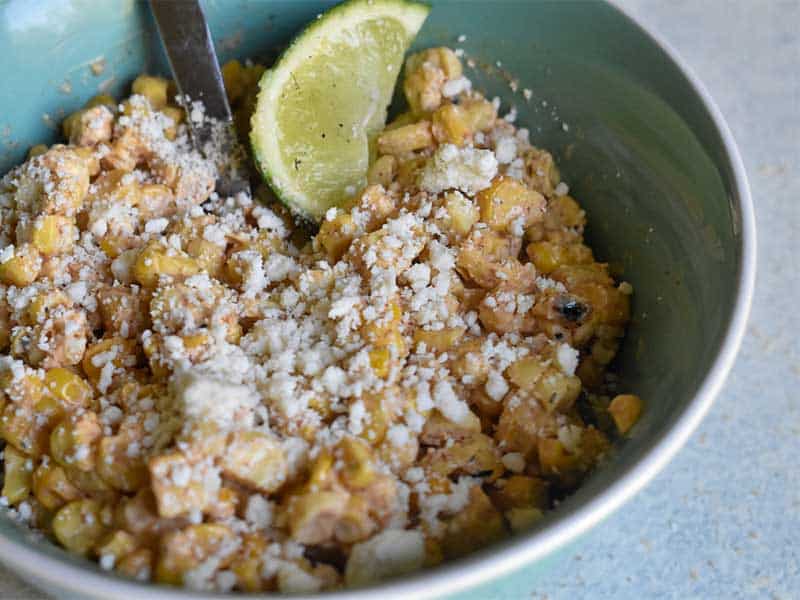 mexican street corn in teal bowl with lime wedge on a white table