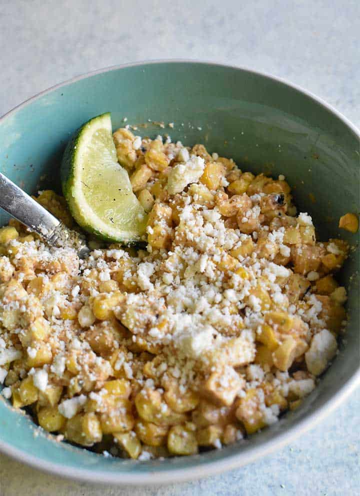 mexican street corn with lime wedge in teal bowl on white table