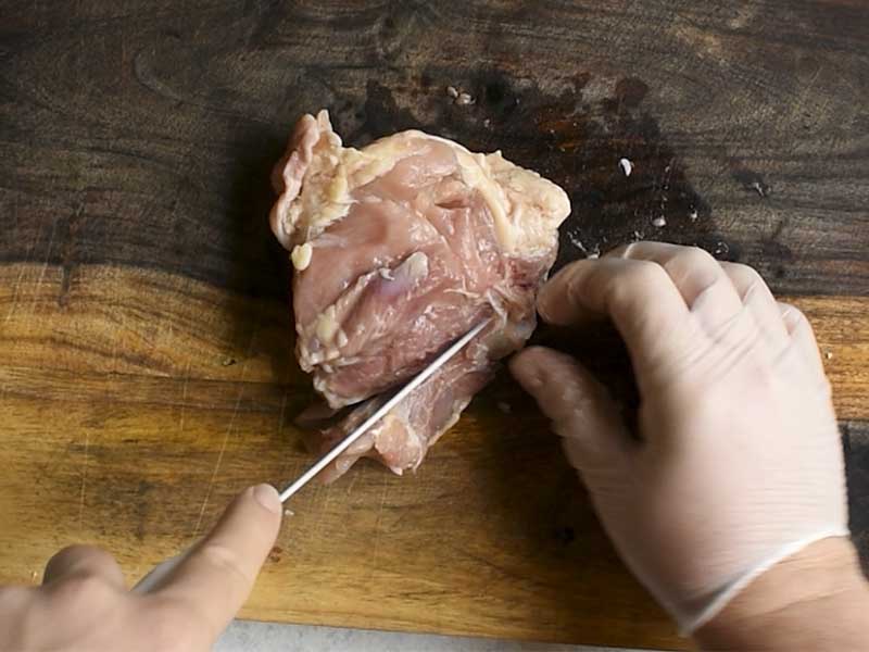 chicken thigh being deboned with a boning knife on a brown wooden cutting board