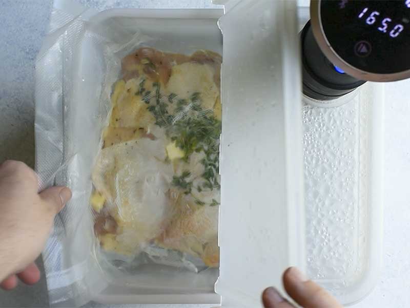 chicken thighs being placed in a clear plastic sous vide container filled with water for cooking