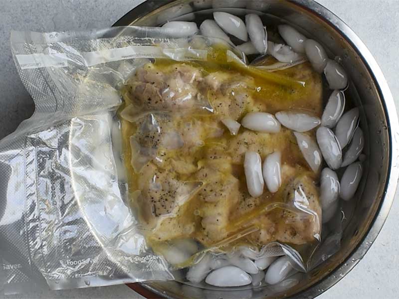 chicken thighs in a bag sitting in a metal bowl filled with ice water