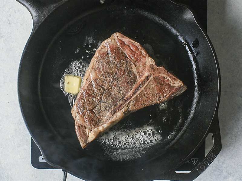 bone in ribeye steak cooking in a black cast iron pan with melting butter