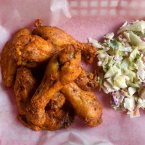 air fryer chicken wings shot from overheat, wings in hot sauce next to a chopped salad in a red basket with a food service papper