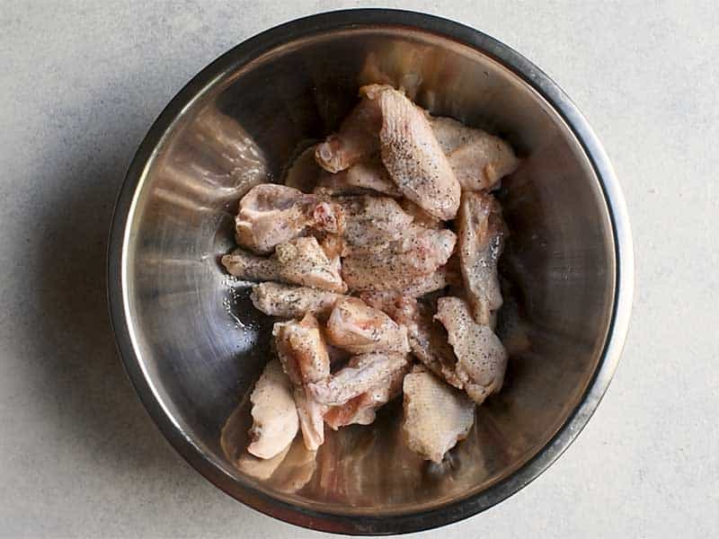 raw chicken wings seasoned with salt and pepper in a metal bowl on a white table