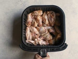 uncooked chicken wings in a black air fryer basket on a white table