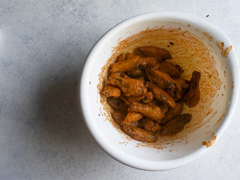 chicken wings tossed in buffalo sauce in a plastic white bowl on a white table