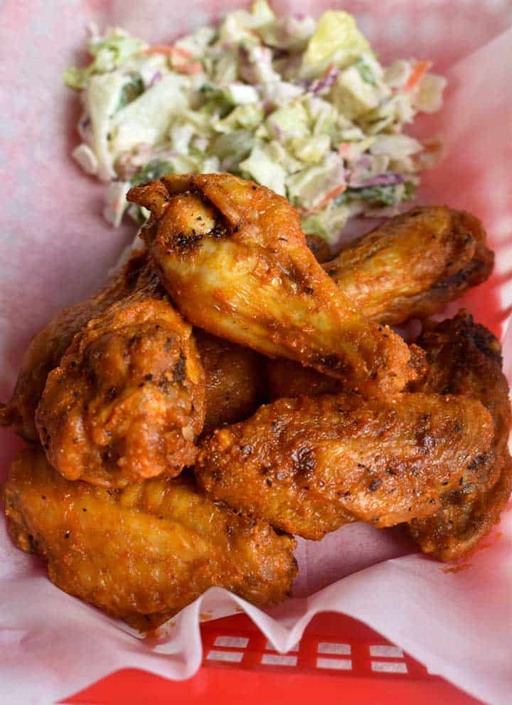 buffalo wings in a red food basket with white paper and a chopped salad in bleu cheese dressing