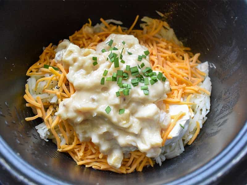 sour cream, chives, potato soup, and hashbrowns sitting in a crockpot for cheesy potatoes