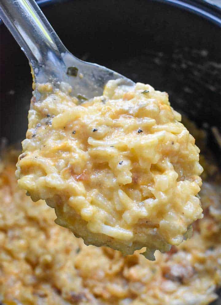 potatoes on a large metal serving spoon above a pot full of cheesy potatoes