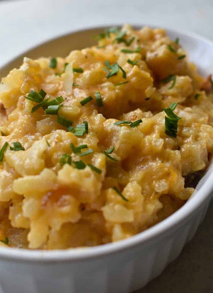 cheesy potatoes in a white dish garnished with chives