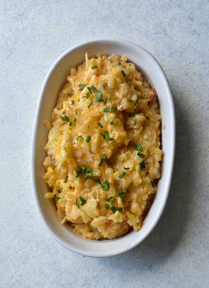 Cheesy potatoes with green chives in a white dish on a white table