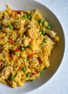 Chicken and yellow rice in a large, shallow white bowl sitting on a white table