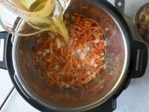 beer being poured into an instant pot with carrots, red peppers and onions