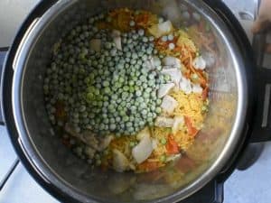 frozen peas on top of cooked chicken and yellow rice inside of an instant pot