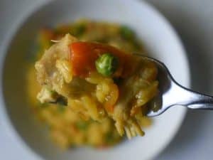 a fork holding arroz con pollo with red peppers and peas. A white bowl with more rice is blurry in the background.