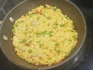 chicken and yellow rice cooking in a small pan on a black cooktop