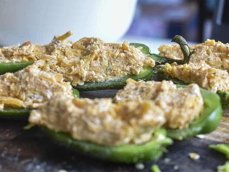 jalapeno peppers cut in half and stuffed with cream and cheddar cheese mixture. Sitting on a wooden cutting board with a white mixing bowl blurry in the background.