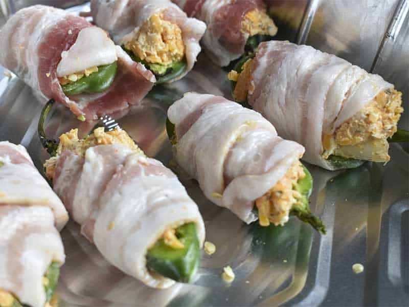 bacon wrapped smoked jalapeno peppers in an aluminum foil tray.