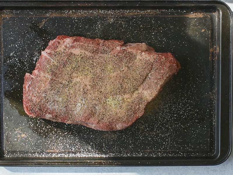 Chuck roast seasoned with salt pepper and garlic in a large baking tray