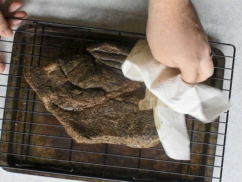 chuck roast that has been cooked in a sous vide being patted dry with a paper towel while sitting on a wire rack above a baking tray.