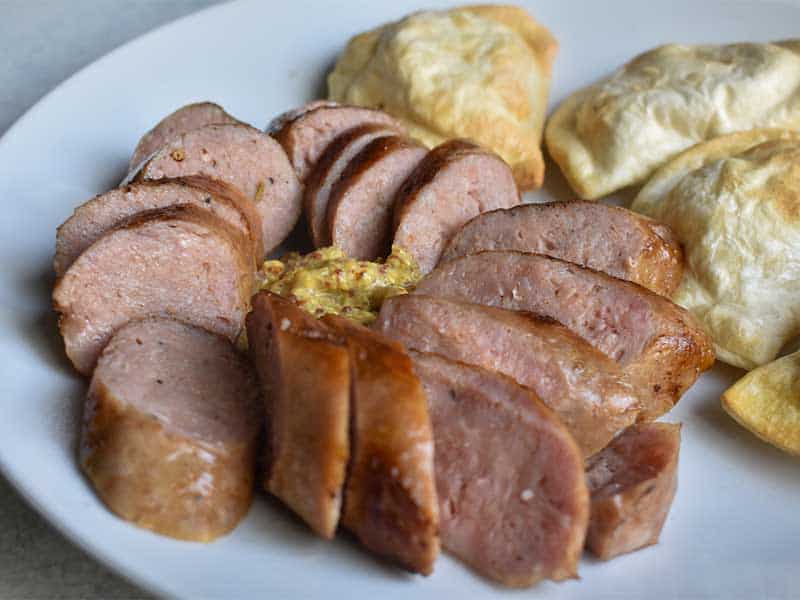 sausage sliced on a white plate with pirogi in the background