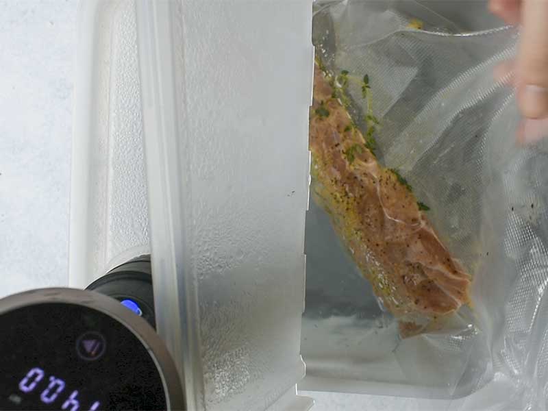 pork tenderloin being lowered into a sous vide container with a hinged lid open