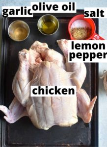 ingredients for air fryer whole chicken which are laid on a dark baking sheet and labeled
