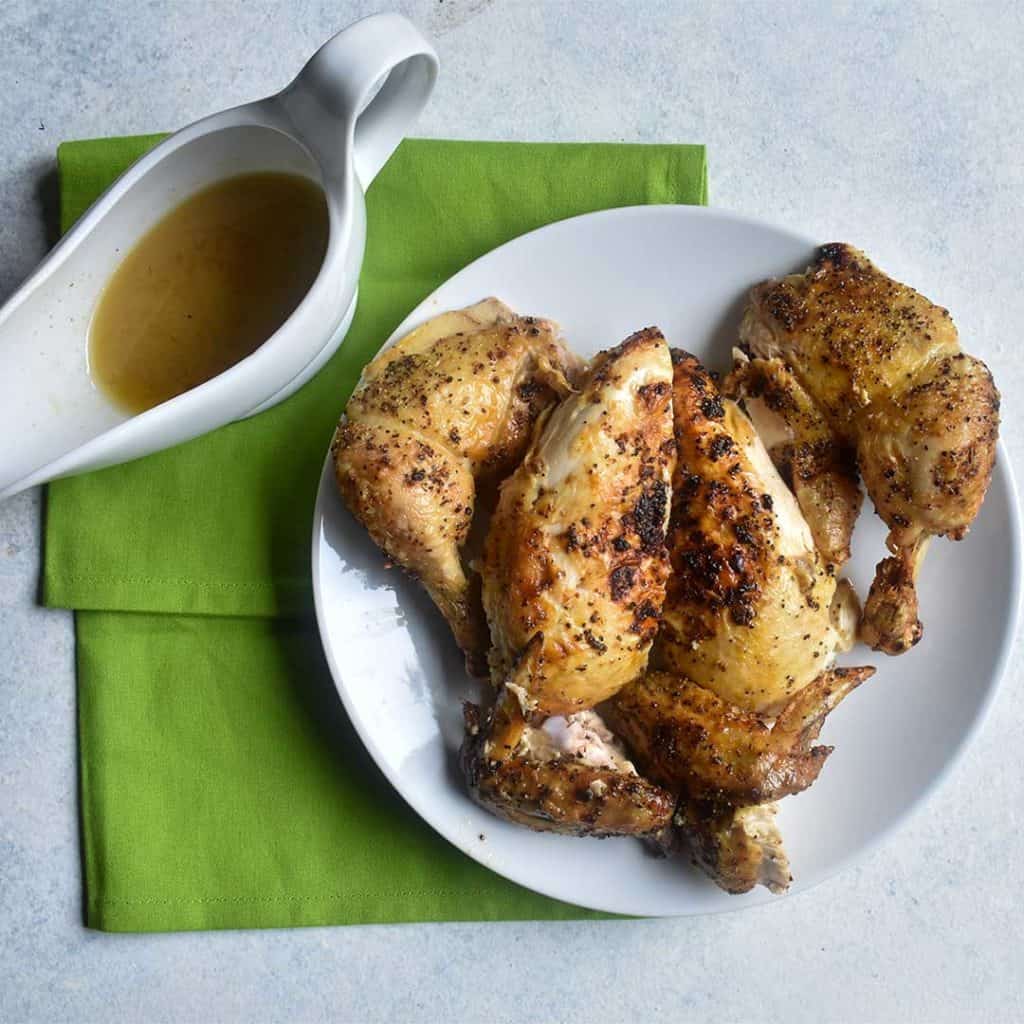 overhead shot of chicken carved on a white plate with a gravy boat and a green napkin sitting on a white table