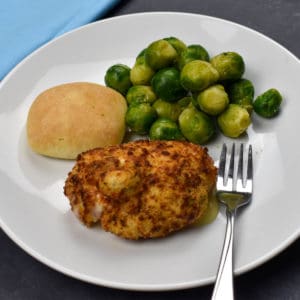 chicken cordon blue on a white plate with a bread roll and brussels sprouts