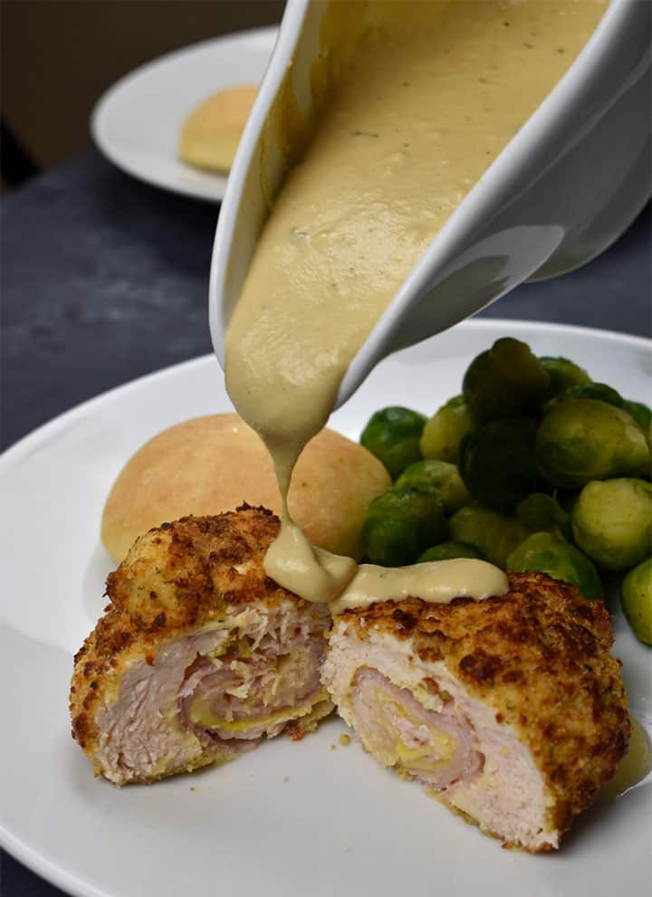 chicken cordon bleu cut in half with a dijon mustard sauce being poured over top.