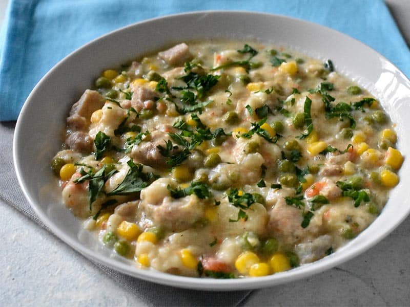 instant pot chicken and dumplings topped with parsley. There are silver and light blue napkins sitting on a white table.