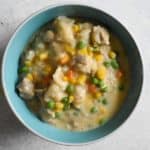 overhead shot of instant pot chicken and dumplings in a light blue bowl on a white table